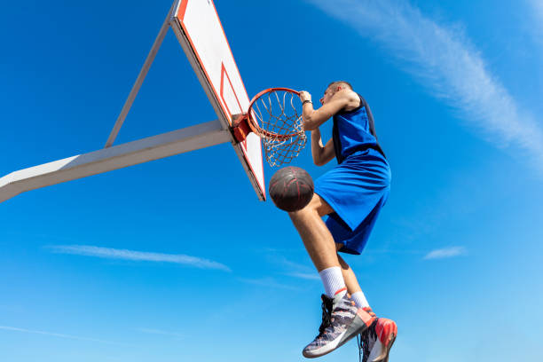 istock Slam Dunk. Side view of young basketball player making slam dunk 950938690