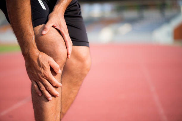 膝の怪我。痛みでランニング トラックでランニング トレーニング トレーニング中の筋肉の損傷に苦しんだ後彼の手と膝を保持している強力な運動脚を持つ若いスポーツ男。 - men anatomy the human body body ストックフォトと画像