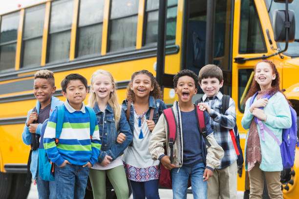 Elementary school children waiting outside bus A group of seven multi-ethnic elementary school children, 7 to 9 years old, standing outside a yellow school bus, carrying backpacks. back to school photos stock pictures, royalty-free photos & images