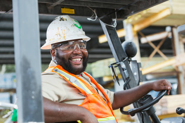 afrikanisch-amerikanischer mann fahren gabelstapler im holzlager - minority african ethnicity business hardhat stock-fotos und bilder