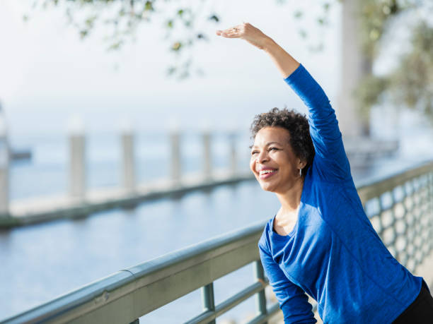 dojrzała afroamerykanka ćwiczy na nabrzeżu - exercising stretching women outdoors zdjęcia i obrazy z banku zdjęć