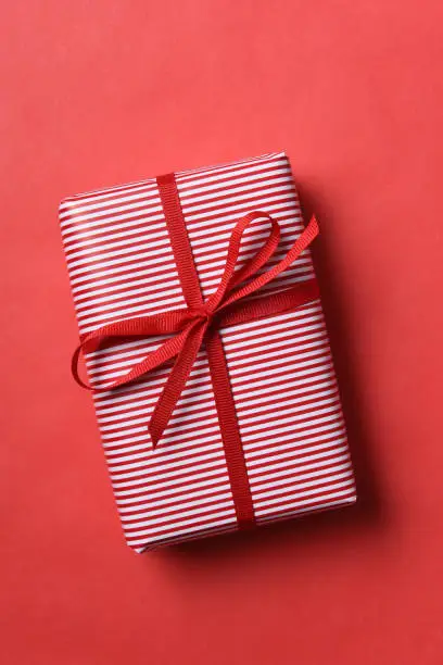 A Christmas present wrapped in red and white striped paper with red ribbon on a red background.