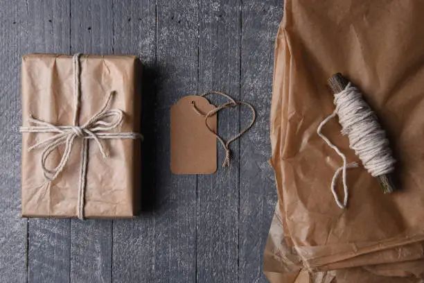 High angle shot of plain brown paper wrapped Christmas gift with blank tag and extra paper and string.