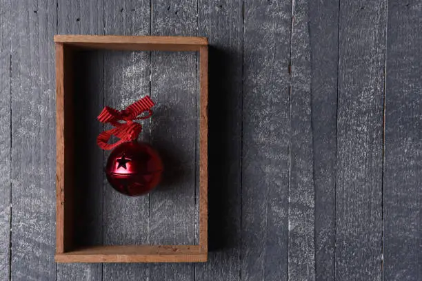 A red jingle bell in a wood frame on gray wood wall with copy space.