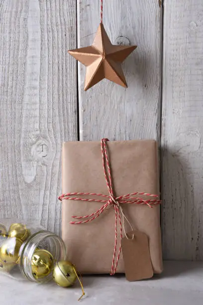 Star hanging over a plain brown paper wrapped Christmas present. The present is leanng on a rustic whitewashed wall.
