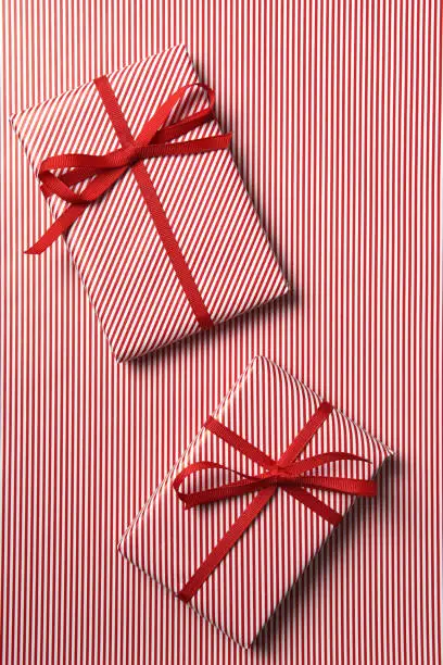 Top view of two Christmas presents wrapped with red striped paper and red ribbon on a background of the same paper.