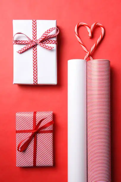 Two Wrapped Christmas presents with matching paper rolls and a candy cane heart.