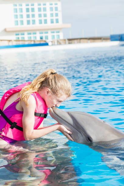 istock Girl standing in water kissing a dolphin 950968986