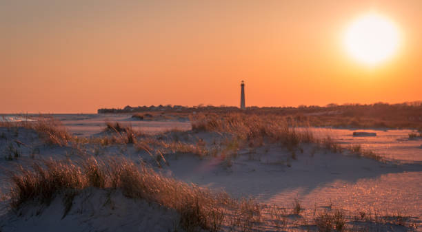 tramonto sulla spiaggia mentre il faro di cape may si trova sullo sfondo - contea di cape may foto e immagini stock