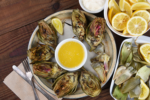 High angle view of a plate full of grilled artichokes with lemons, butter and mayonnaise, with a plate for the eaten leaves.