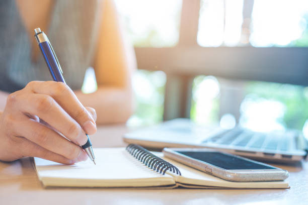 istock Business woman hand is writing on notepad with pen in office.On her desk there is a notebook and a mobile phone. 950985636