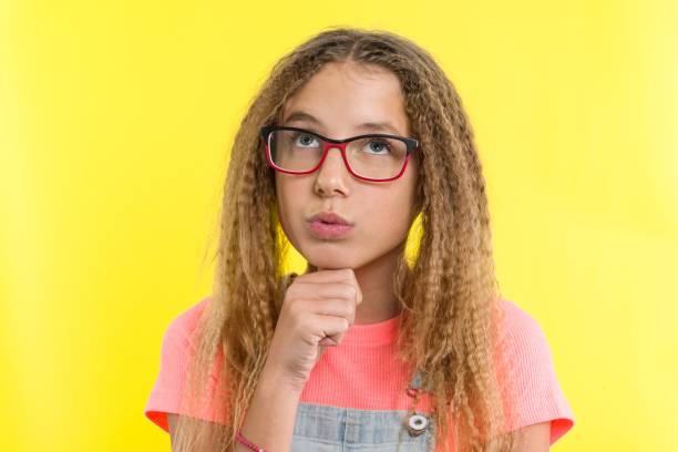 pretty girl 12-13 years old blonde with curly hair with glasses, looks pensively aside, thinking about school. facial expressions concept, yellow background - 12 13 years pre adolescent child female blond hair imagens e fotografias de stock