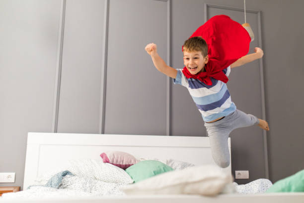Happy boy flying like a superman in a bedroom.