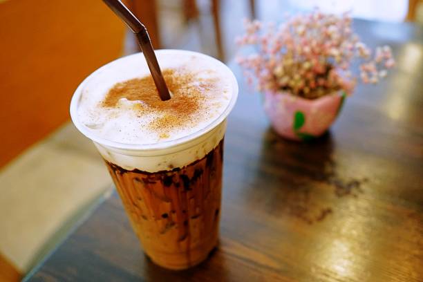 un café de moka glacé au lait mousse garni de cannelle en poudre placé sur la table en bois brun foncé. boisson dans la tasse en plastique. - foamed milk photos et images de collection