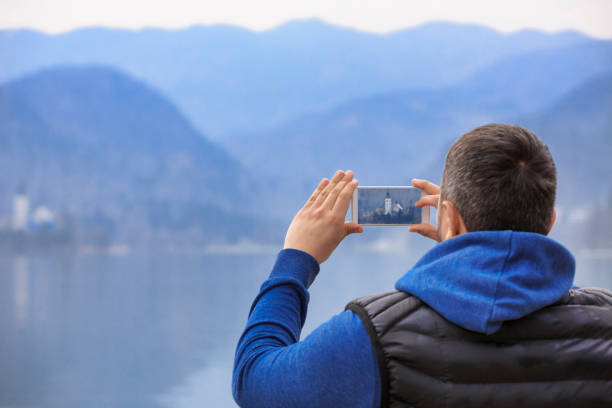 istock Men tourists, using smartphone, Photo Messaging and browsing the internet. Enjoying the view of  on the Lake Bled, Slovenia, Europe. 951016832