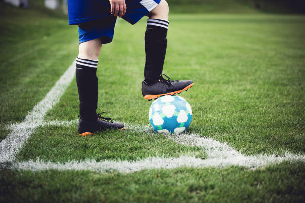 kind im örtlichen stadion außerhalb auf wiese fußball zu spielen. schuss zu senken, füße und kugel hautnah. kinder spielen fußball, lieblingssport, fußball fieber weltweit. - soccer shoe soccer player kicking soccer field stock-fotos und bilder