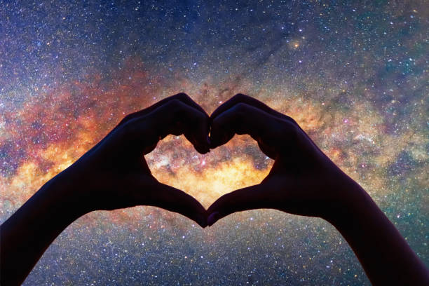 Silhouette heart shape hands with milky way in the night sky background.