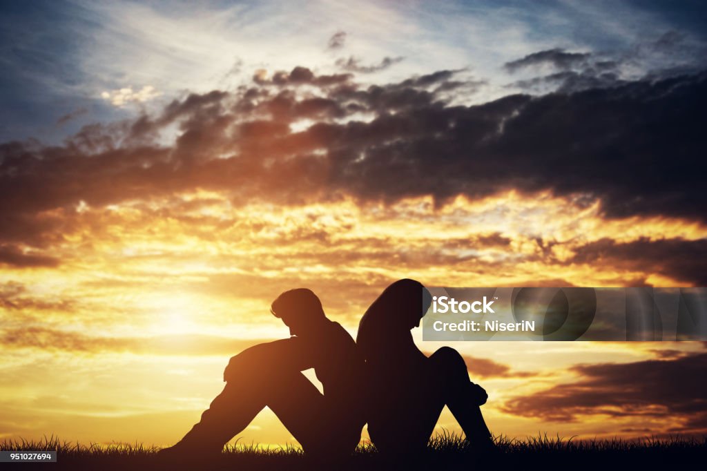 Sad couple sitting back-to-back on a ground. Couple - Relationship Stock Photo