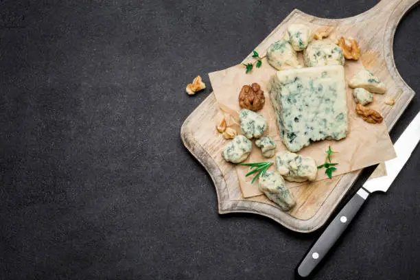 Slice of French Roquefort cheese on wooden cutting board