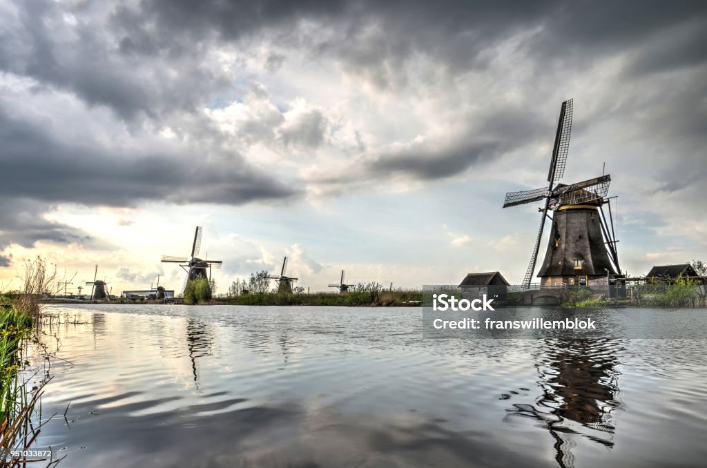 Clouds over a canal in Kinderdijk Partially cloudy sky and several historic windmills relfecting in a canal at Kinderdijk Unesco world heritage site Beauty Stock Photo