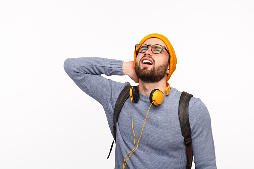 Casual man in yellow hat with headphones holding neck and looking up on white background.