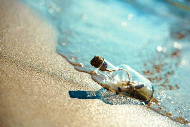 istock A bottle with a message is thrown by a wave on a sandy beach. Sandy background. The bottle floats in the surf line 951044360