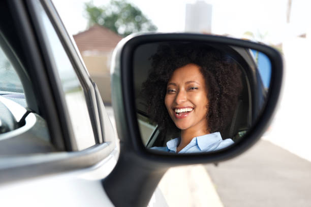 riflessione nello specchio laterale di sorridente donna africana alla guida auto - reflection women contemplation ethnic foto e immagini stock