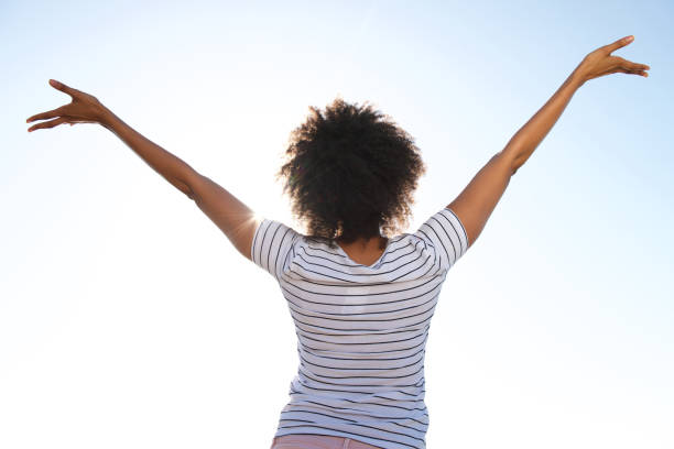 istock young female standing outdoors against sky with her hands raised 951045194