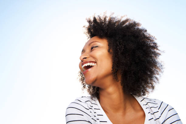 istock cheerful young black woman laughing outdoors against bright sky 951045200