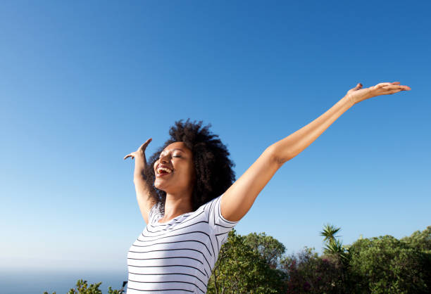 young african woman standing outdoors with arms raised and laughing stock photo