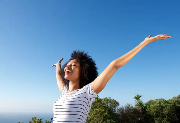 Photo of young african woman standing outdoors with arms raised and laughing