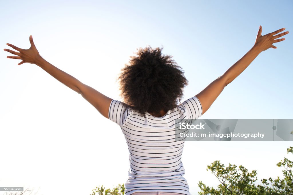atrás do jovem mulher olhando para o sol com os braços levantados - Foto de stock de Mulheres royalty-free