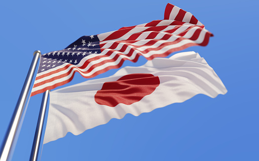 High quality 3d render of American and Japanese flags waving with wind on a blue sky. Low angle view with copy space and selective focus.