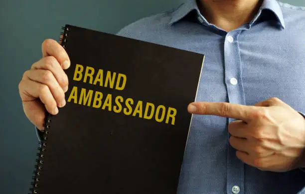 Photo of Man is holding book with title Brand Ambassador.