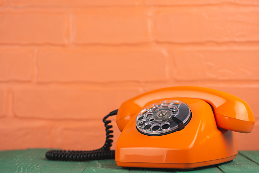 Old vintage orange phone on brick wall background
