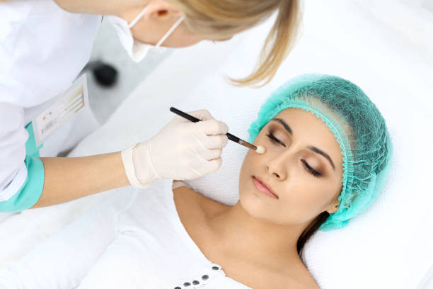 istock Professional beautician is doing cosmetic procedure at light medical background touching patient's face with brush, closeup.  Cosmetology treatmen 951054996