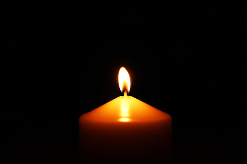 Big single candle in the center of the photo on dark background. Memory calm glow light closeup. Romantic or RIP darkness template