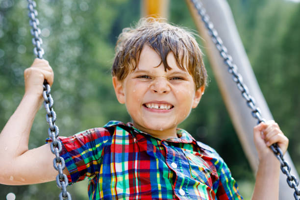 istock Funny kid boy having fun with chain swing on outdoor playground while being wet splashed with water 951059342