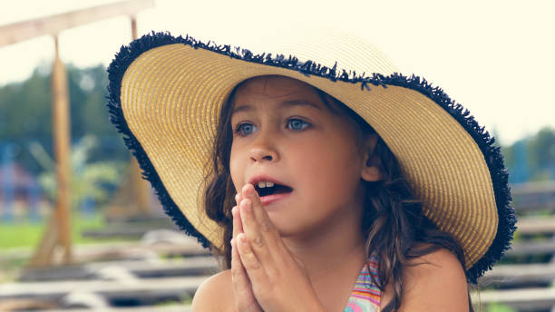 linda menina com um chapéu à beira-mar dobrado suas mãos em oração e olha para a distância - child praying beach little girls - fotografias e filmes do acervo
