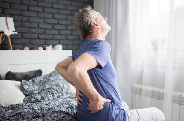 Senior man with lower back pain siting on bed Portrait of senior man with lower back pain siting on bed lower back pain stock pictures, royalty-free photos & images