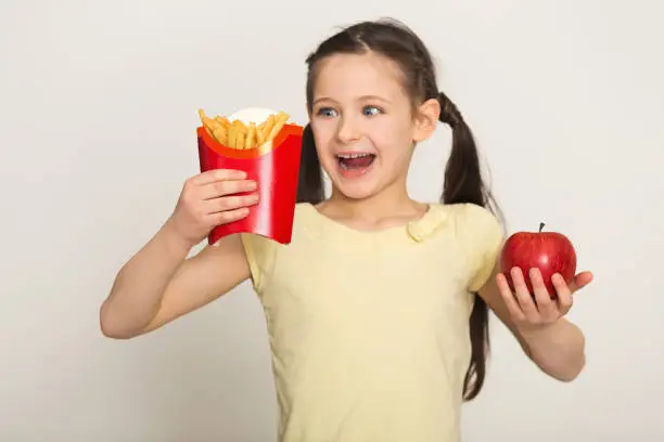 Photo of Happy little girl holding a bag of fries and apple