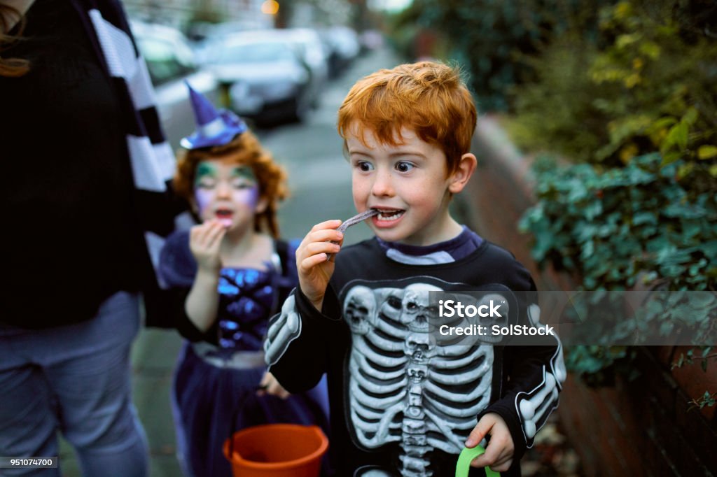 Eating Halloween Candy Little boy eating halloween candy while trick or treating in suburban streets with his mother and sister. Halloween Stock Photo