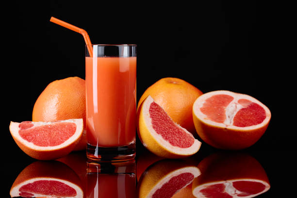 Glass of  grapefruit juice and cut fruits on black background.
