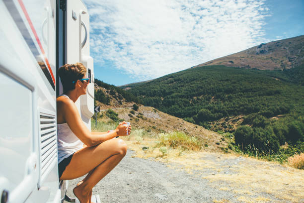 Girl sits on a motor home step Side view of a young woman is sitting on a caravan step and holding a cup on a holiday adventure trip stop. Copy space area available mobile home stock pictures, royalty-free photos & images