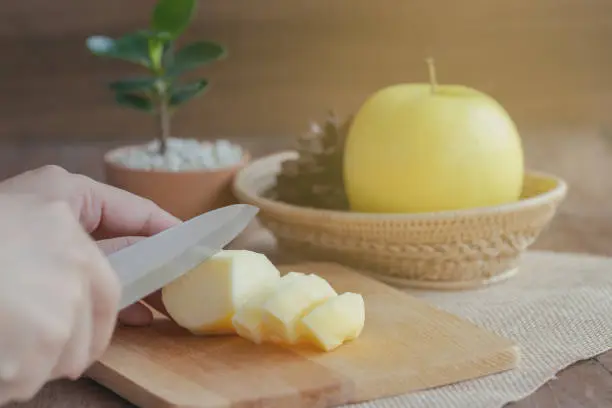 Woman use knife kitchen to chopped or cut and sliced fresh Shinano gold apple on wood cutting board under sunlight for snack and salad or prepare for homemade apple pie for family.Home cooking concept