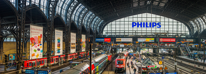 Panoramic view across the trains, platforms and commuters under the wrought iron arches of Hamburg’s Hauptbahnhof central railway station, Germany.