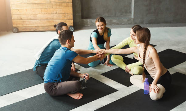 Young men and women in circle with united hands. Young men and women sitting in circle with united hands before training. Togetherness and support, youth sports fashion and active lesiure. Pov, copy space teenage yoga stock pictures, royalty-free photos & images