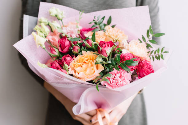 giovanissime donna con in mano un colorato bouquet di fiori freschi in fiore di diversi tipi di rose, garofani, eustoma, peonie sullo sfondo grigio della parete - composizione di fiori foto e immagini stock