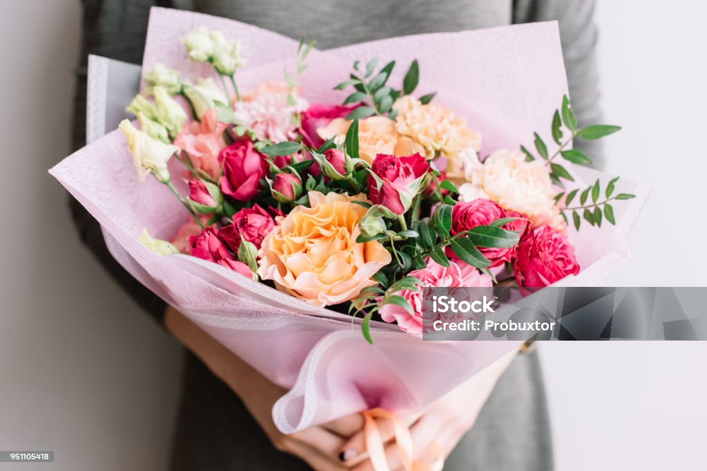 Very nice young woman holding a colourful fresh blossoming flower bouquet of different sorts of roses, carnations, eustoma, peonies on the grey wall background Flower Stock Photo