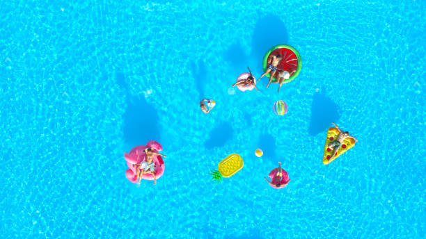 aerial glückliche junge freunde spielen mit einem ball auf lustige bunte floaties im pool - men sensuality photography high angle view stock-fotos und bilder
